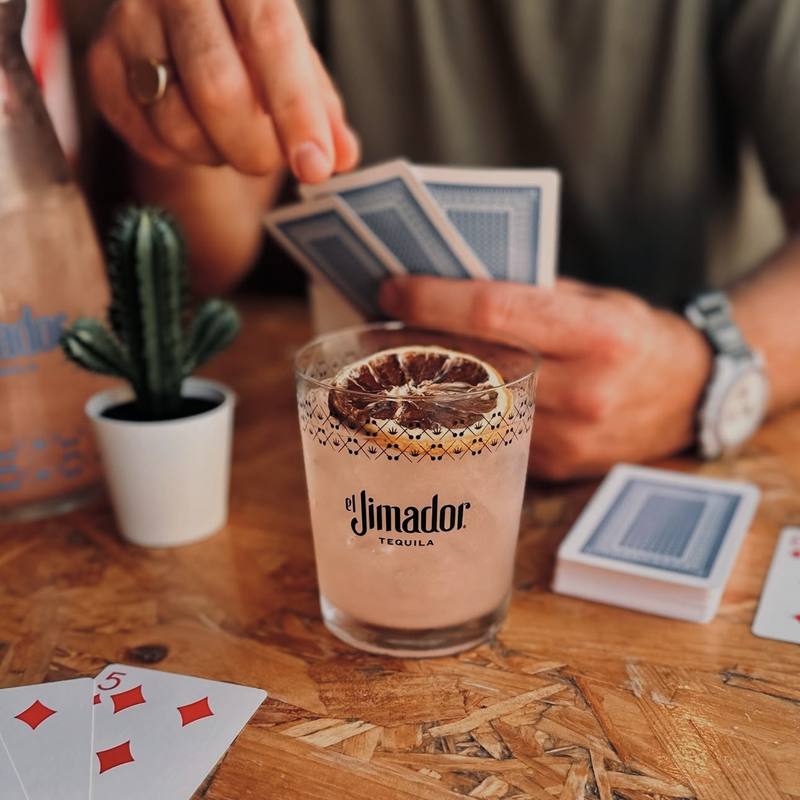 Tequila cocktail with a dried orange slice beside a cactus and playing cards