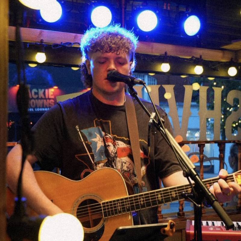 Singer playing acoustic guitar on stage under blue lights